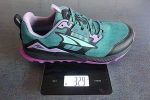 Altra Lone Peak 7 Review (2026 Report After 90-Mile Hike) Teal-and-black Mizuno trail running shoe with pink accents rests on a digital scale reading 329 grams, highlighting its lightweight design.