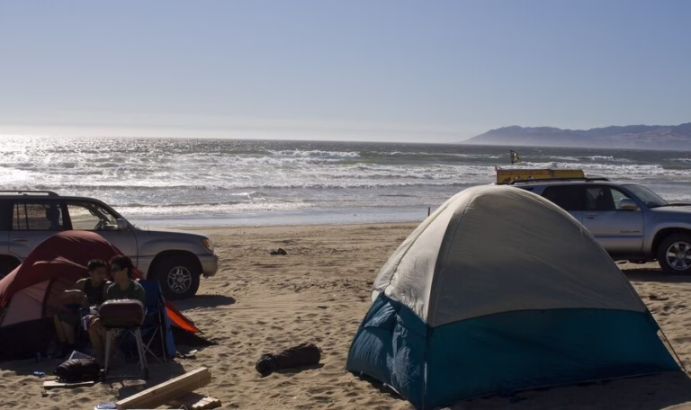 two boys on beach camping with tent and cars at the background