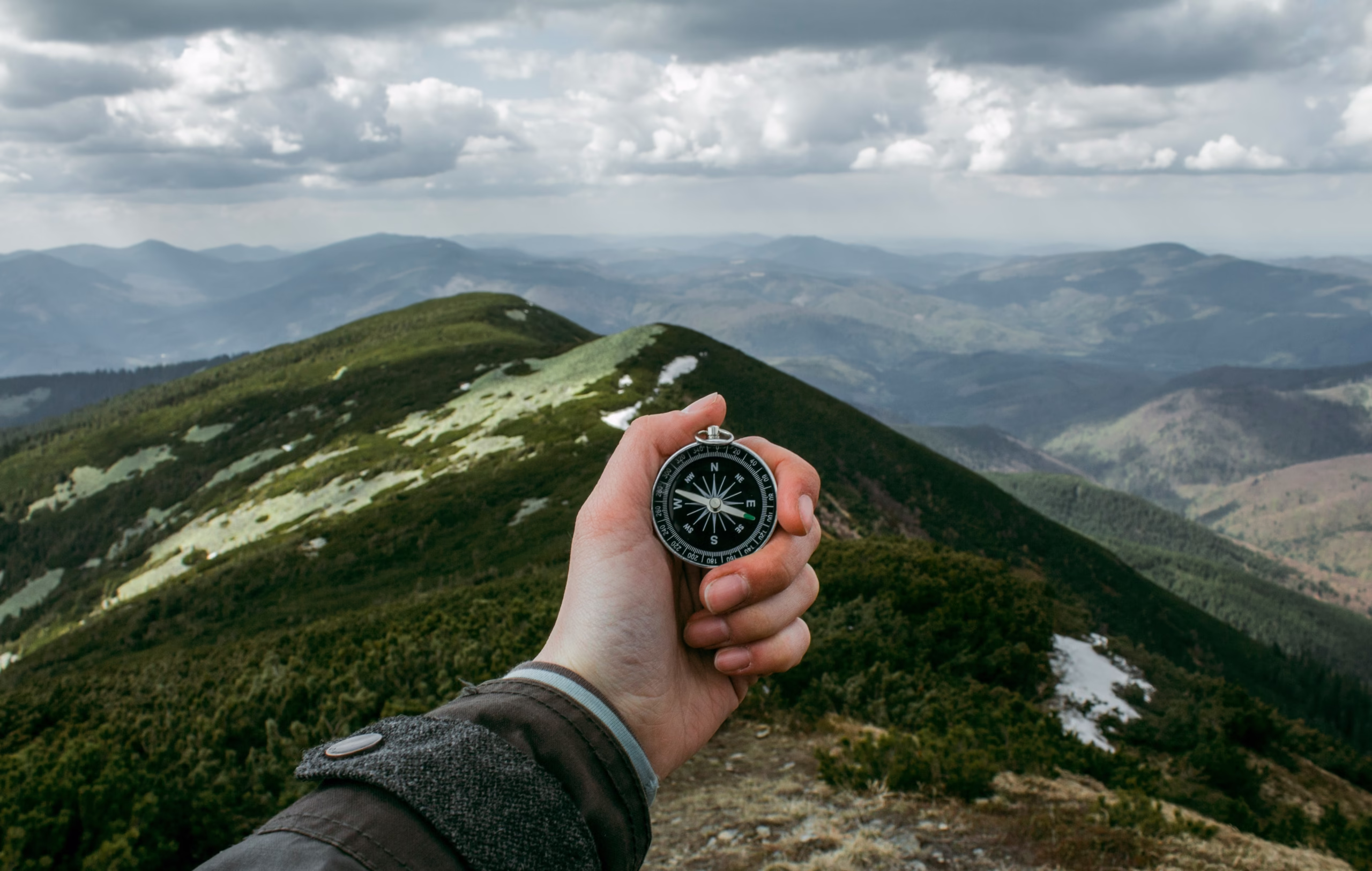 Holiday Gifts for Hikers: 15 Perfect Ideas for Every Budget a compass being held out on the back of a mountain range