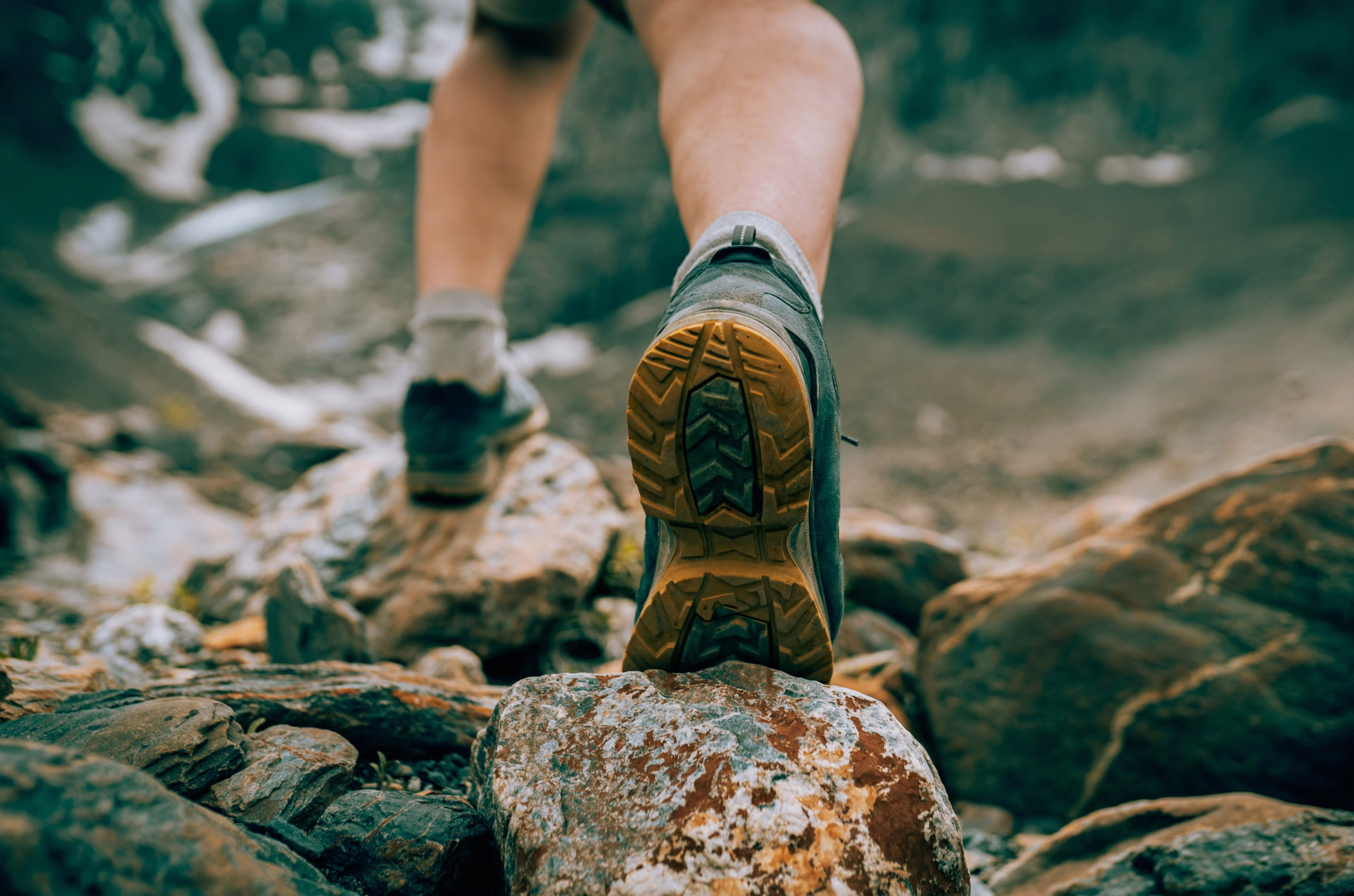 The Ultimate Outdoor Footwear Guide (All Types Explained & More) Close-up of a hiker's boots on rocky terrain, capturing the action of climbing. The scene conveys adventure and determination in a mountainous landscape.