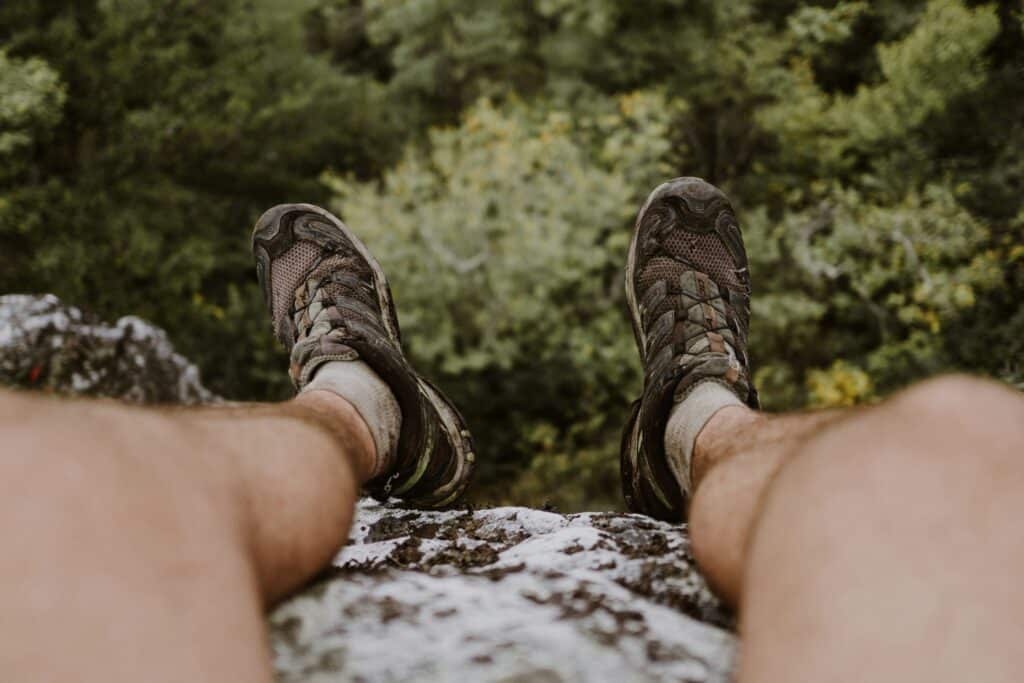 Hiker's legs in brown hiking shoes resting on a rock ledge above a forested valley