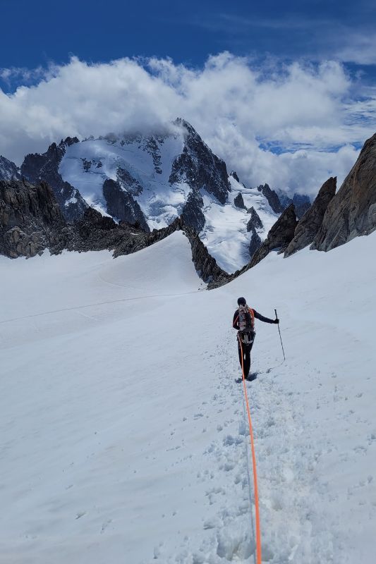 Mountaineering Beginners Guide: Preparing Your First Ascent A hiker ascends a snowy, slopy mountain trail, carrying a backpack against a backdrop of white snow.