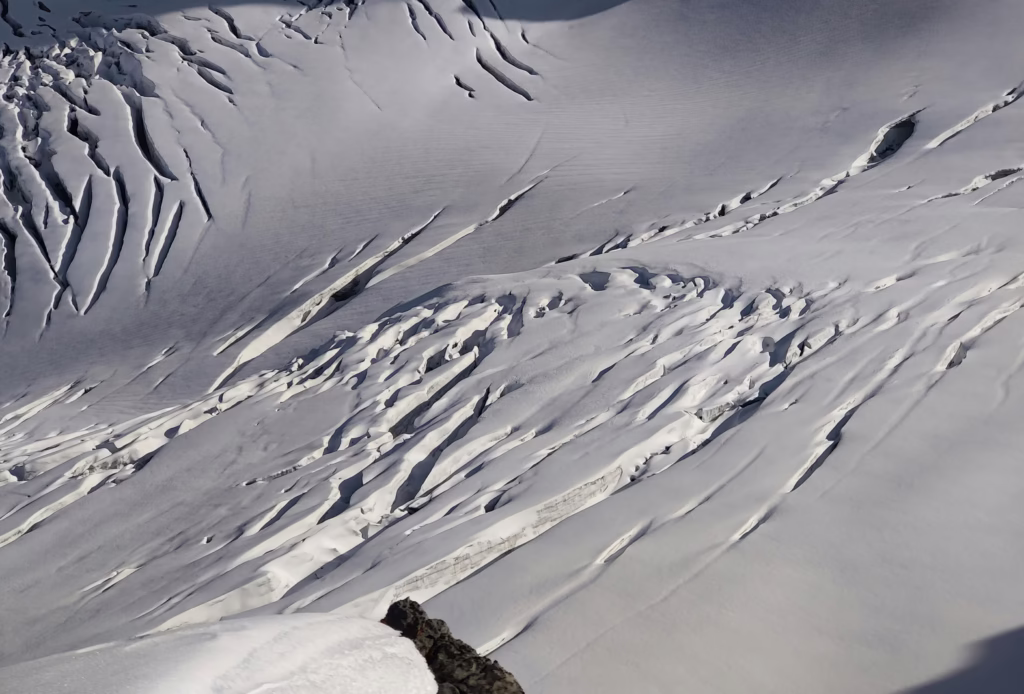 Mountaineering Beginners Guide: Preparing Your First Ascent A vast snow-covered mountainside with deep crevasses and ridges under diffused light, conveying a stark and serene winter landscape.