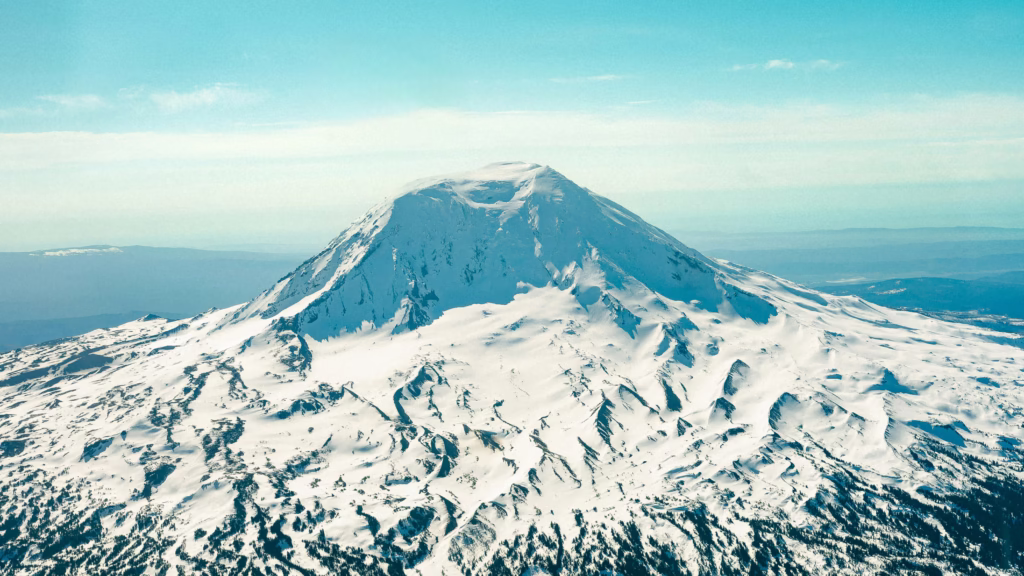 Mountaineering Beginners Guide: Preparing Your First Ascent Snow-covered mountain under a clear blue sky, with rugged peaks and ridges. The landscape conveys a serene, majestic, and chilly atmosphere.