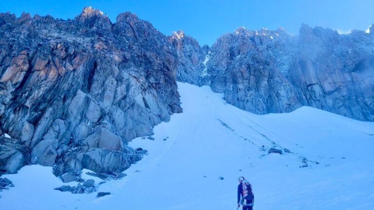 Mountaineering Beginners Guide: Preparing Your First Ascent A person stands on the edge of a mountain, overlooking a vast landscape of peaks and snow in the distance.