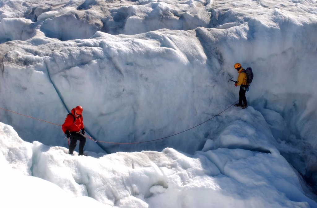 Mountaineering Beginners Guide: Preparing Your First Ascent Two climbers in bright gear navigate a snowy crevasse on a glacier, connected by a rope. The scene conveys caution, teamwork, and adventure.