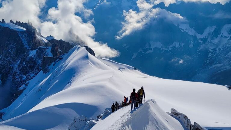 Alpinism vs. Mountaineering: Key Differences Explained A group of people stands on a snowy mountain top, surrounded by clouds in the background.