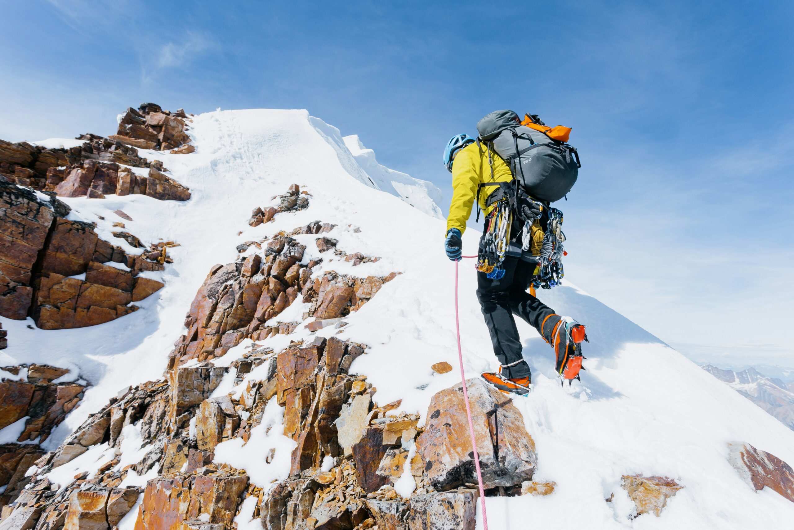 Alpinism vs. Mountaineering: Key Differences Explained alpinist with crampons walking up an icy slope carrying rope and gear