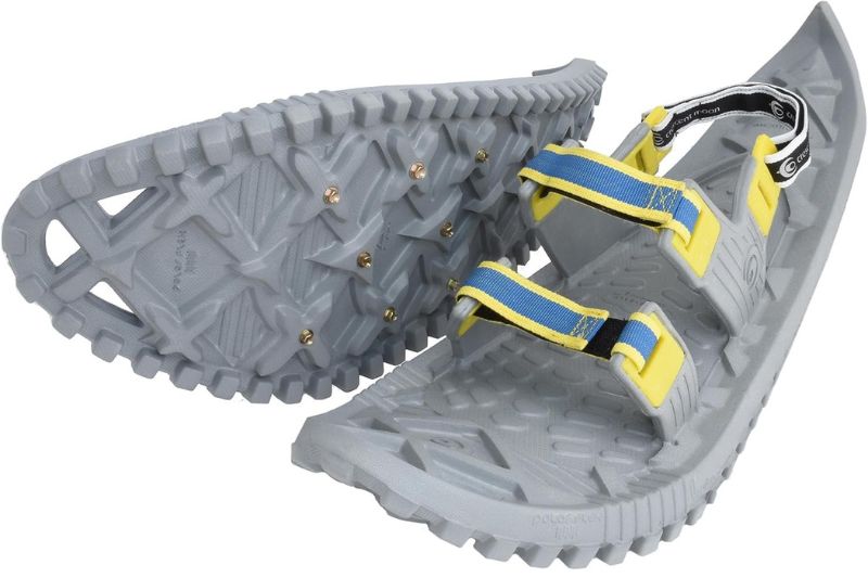 7 Best Snowshoes For Winter Hiking & Mountaineering Gray snowshoes with yellow and blue straps, featuring textured grips and metal studs on the bottom for traction, displayed against a white background.
