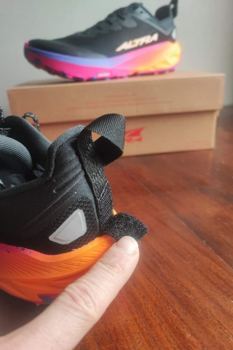 A thumb holding open the velcro tab on the heel of the Altra Experience Wild 3