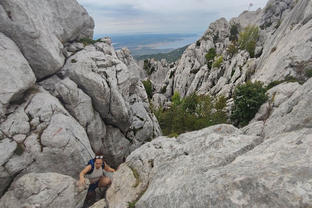 2026 Ultralight Gear Trends: The End of "Stupid Light"? A hiker scrambles up a steep rocky gully on a coastal mountain, hands and feet working the limestone.