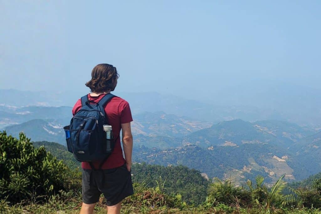 Hiker with two water filter bottles in the side pockets of a daypack, looking out over a hazy valley