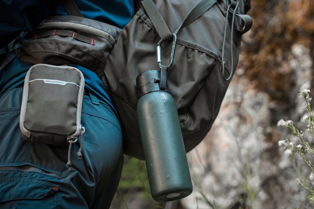 2026 Ultralight Gear Trends: The End of "Stupid Light"? A filtration water bottle hanging from a hikers backpack. It is attached via a carabiner.