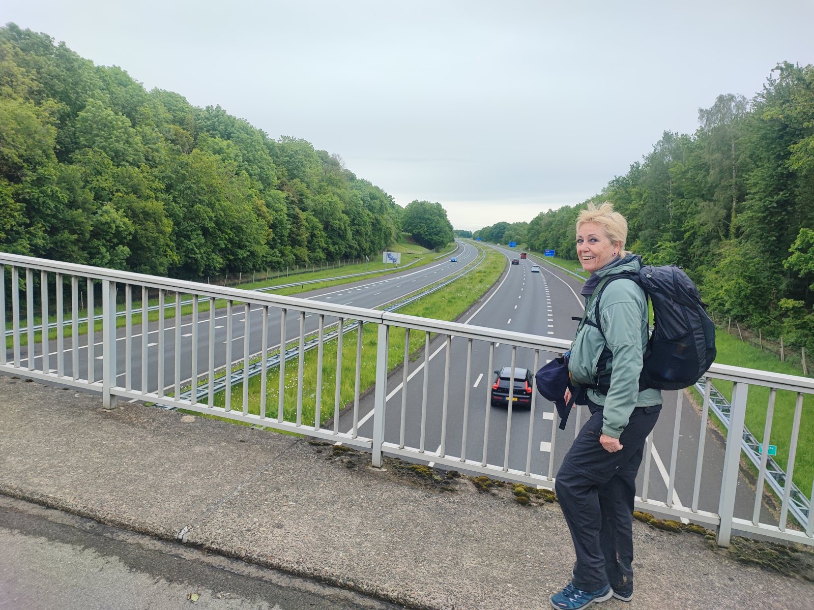 I Walked Four Days of the Pieterpad Without Booking a Single Bed Hiker with a pack standing on a footbridge over a motorway, woodland on both sides.