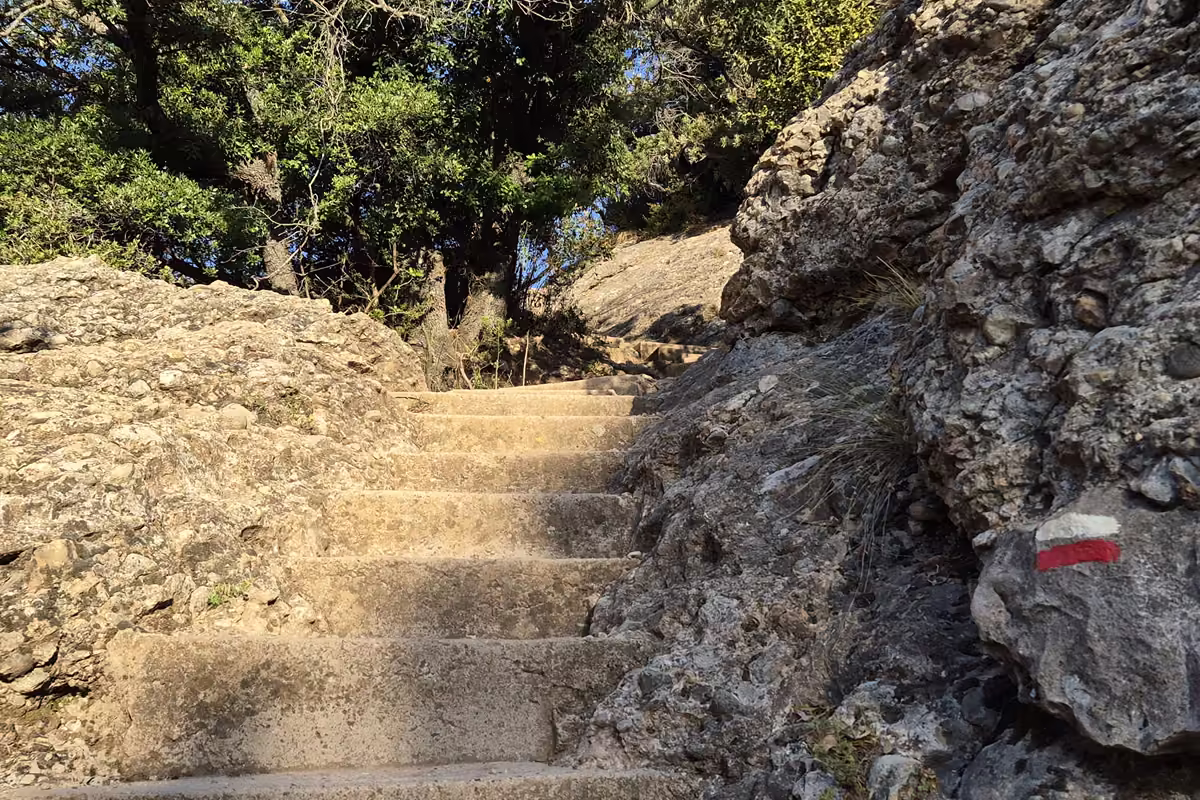 Worn stone steps of the Escales dels Pobres climbing between rock walls, with a red and white GR waymark painted on a boulder.