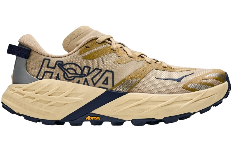 HOKA Speedgoat 7 trail running shoe in tan with a navy HOKA logo and Vibram outsole, side view
