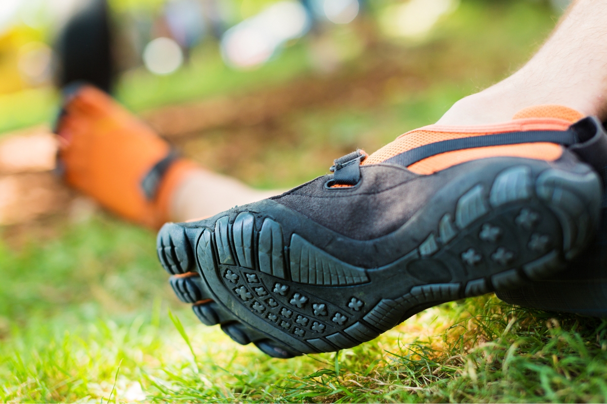 Are Barefoot Shoes Good for You? 5 Clinicians Weigh In (2026) Close-up of the thin rubber sole and separate toe pockets of a black and orange five-toe minimalist shoe on grass
