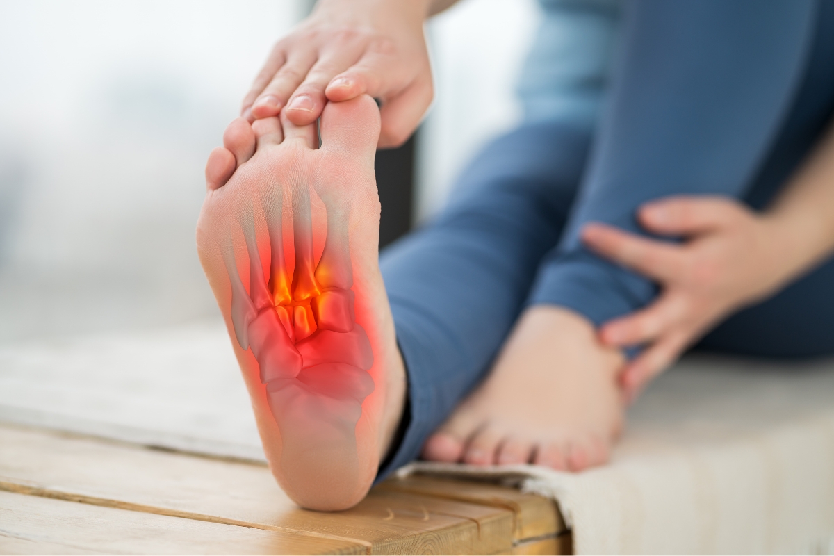 Are Barefoot Shoes Good for You? 5 Clinicians Weigh In (2026) Person holding up the sole of a bare foot, with a red overlay showing pain over the metatarsal bones