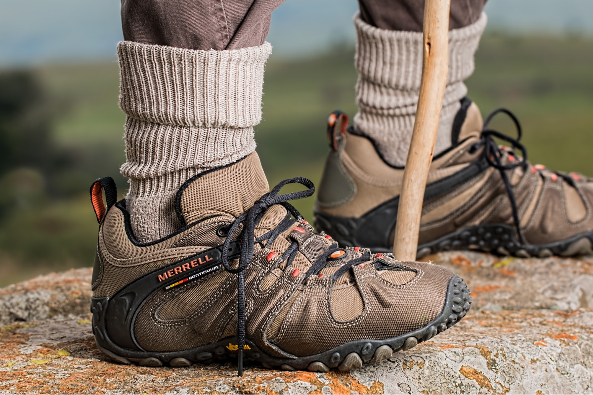Are Barefoot Shoes Good for You? 5 Clinicians Weigh In (2026) Hiker in low-cut hiking shoes and thick wool socks standing on a lichen-covered rock beside a wooden walking stick